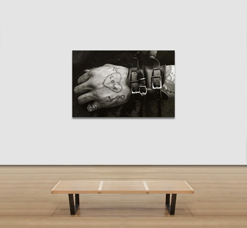 View in a room of a Black and white photograph of a male hand with leather bracelets and a tatoo. Limited edition print. Title: Hells Angels' Tatooed Hand at the Isle of Wight 1970 Festival
